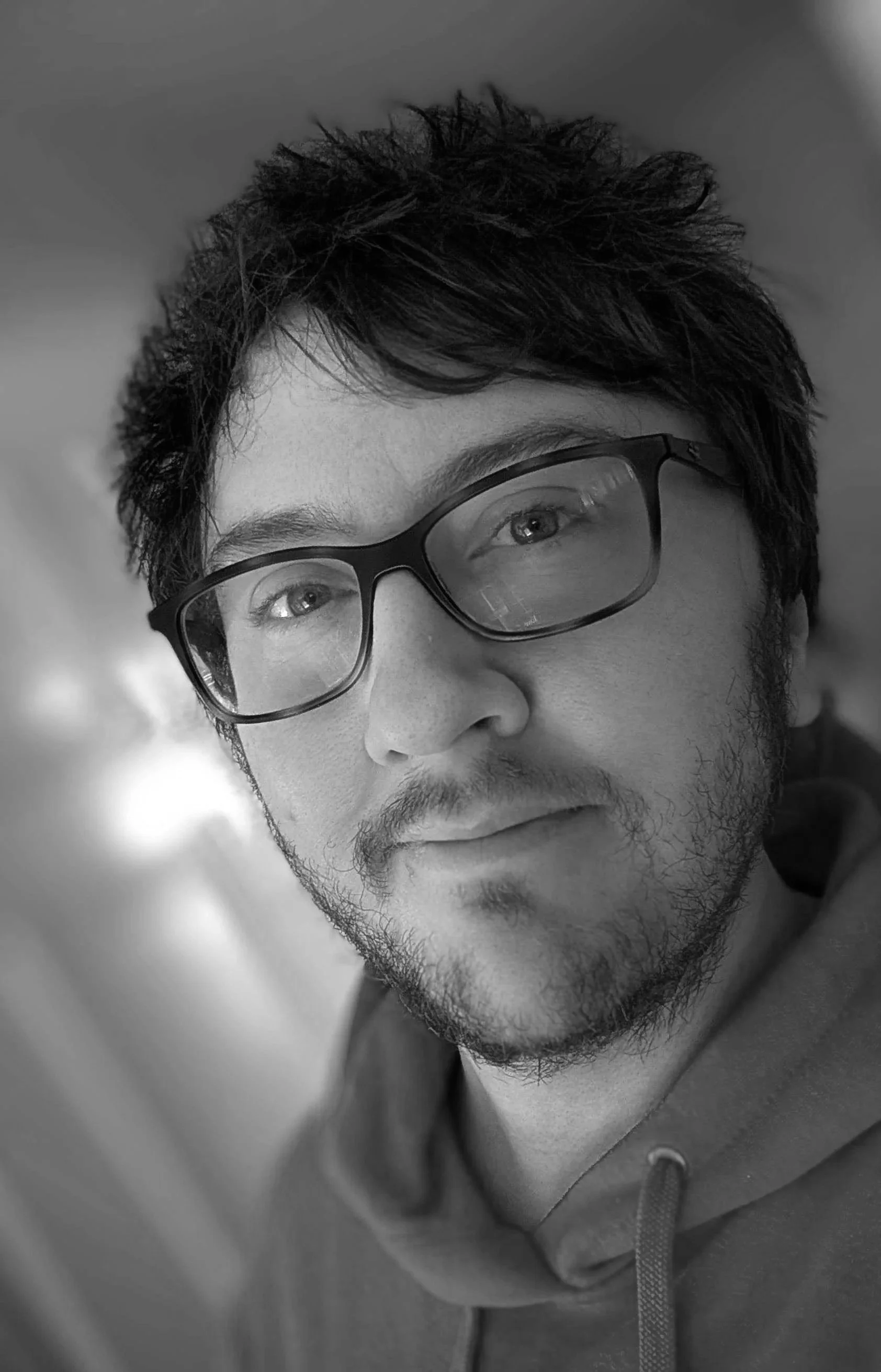 A man with brown hair and beard wearing rectangular glasses and a red top.