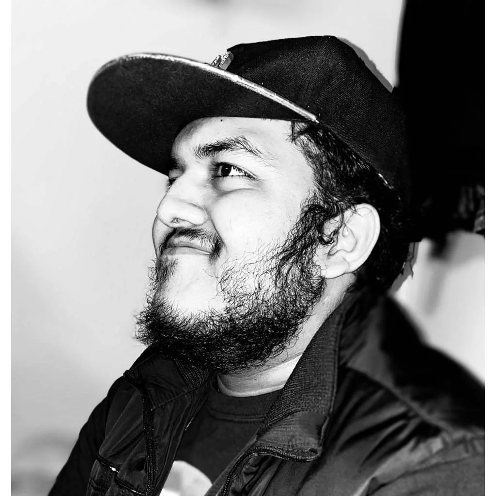 A man with a beard wearing a trucker hat and jacket.