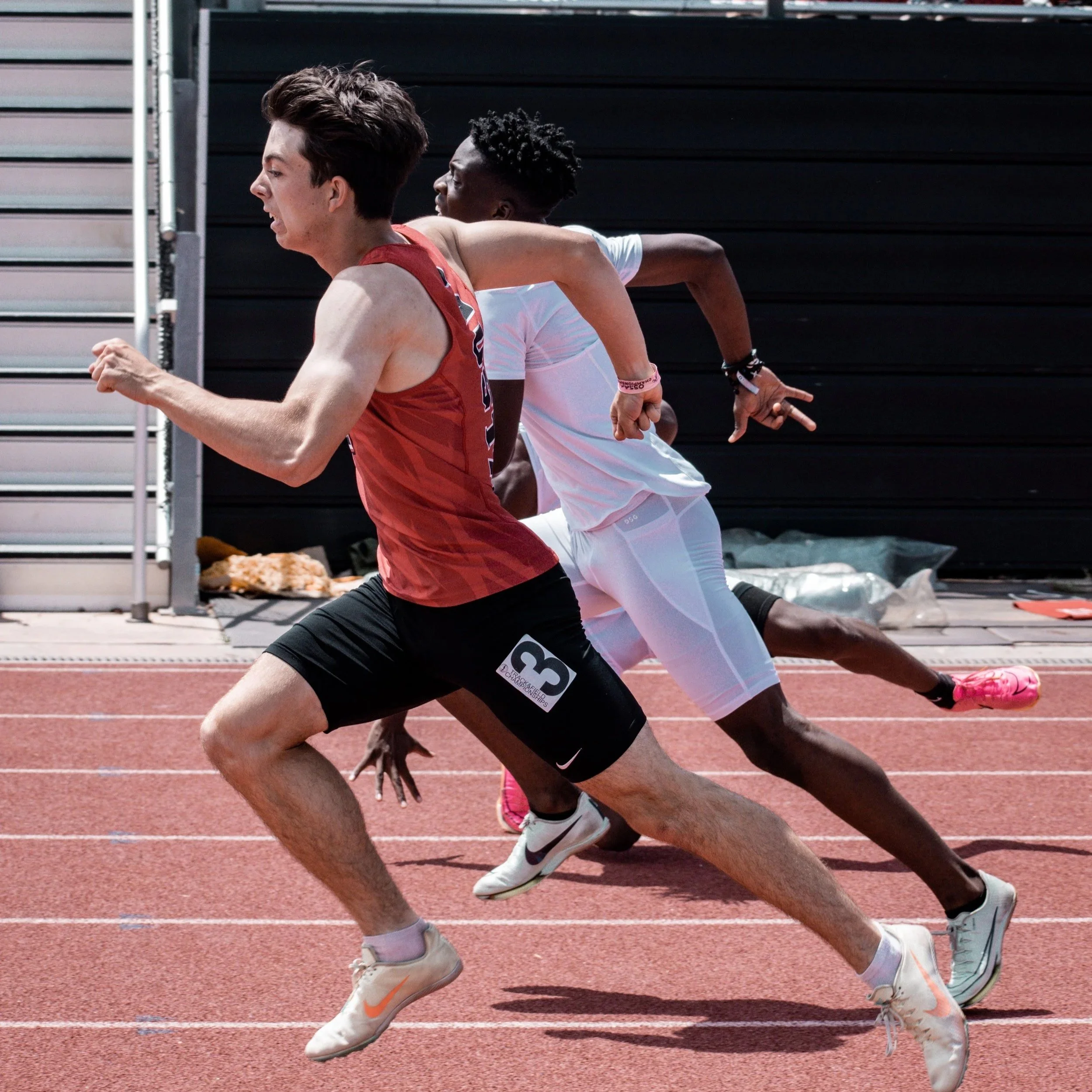 Three male sprinters running on a red track during a race.