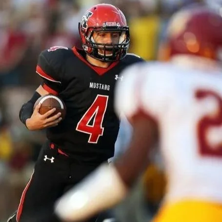 An American football player in a black and red uniform holding a football, looking forward on the field.