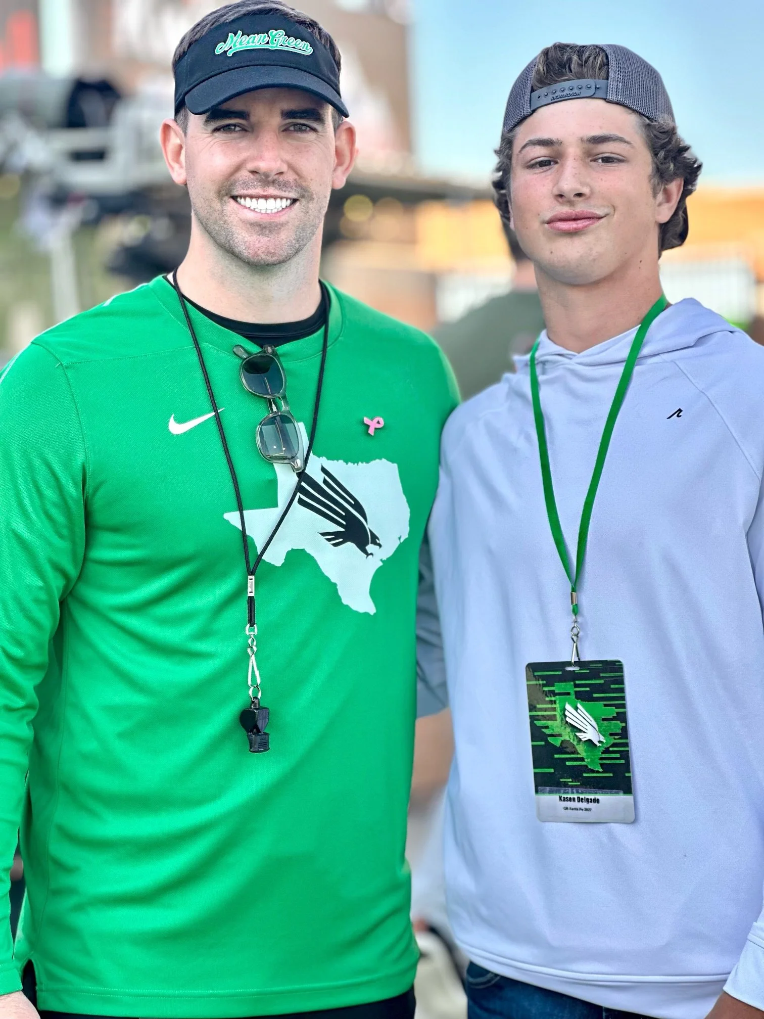 Two men standing outdoors wearing athletic clothing and lanyards, smiling at the camera.