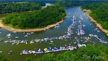 Boats and vehicles docked along the edge of a river, with a river course winding through green trees and grassy areas.