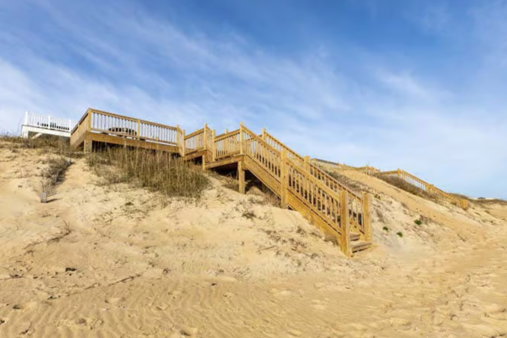 Wooden stairway leading up a sandy beach hillside with a blue sky in the background.