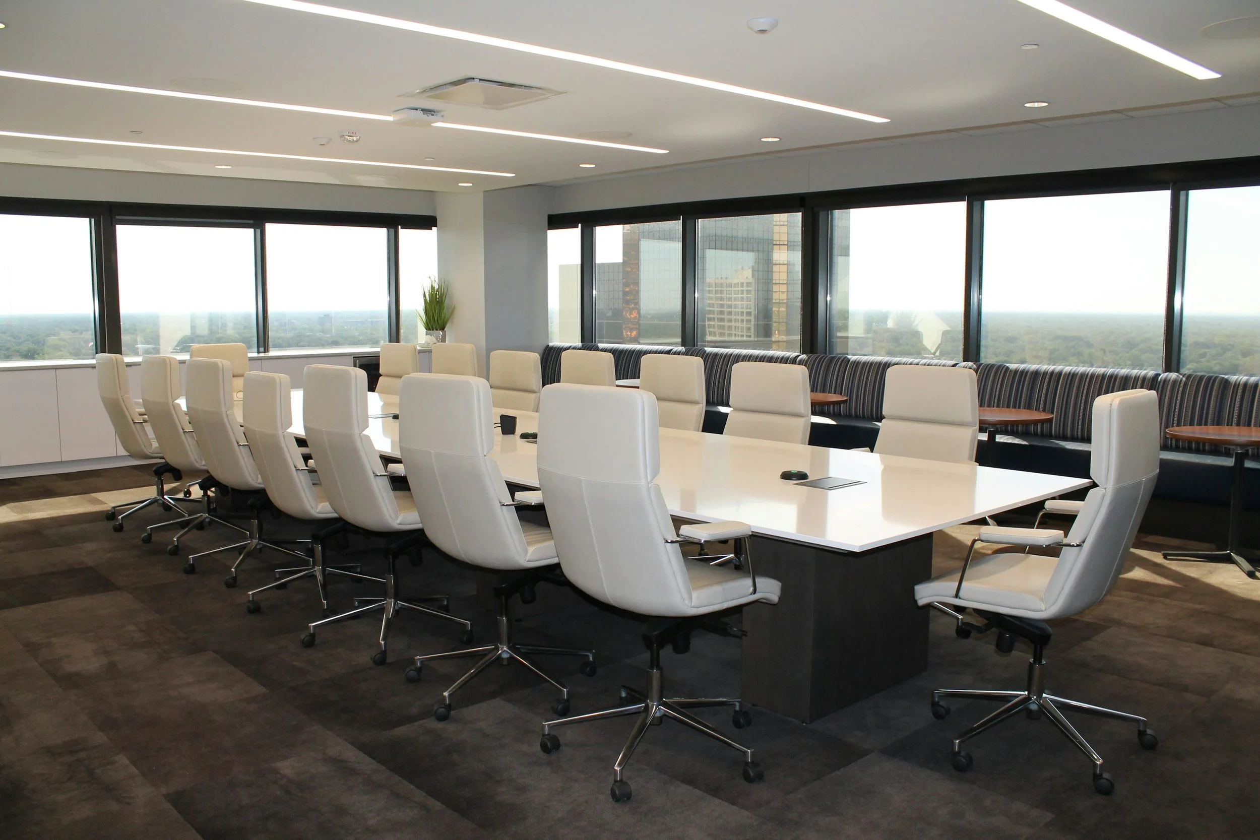 Modern office conference room with a large white table, multiple white office chairs, and large windows with city view.