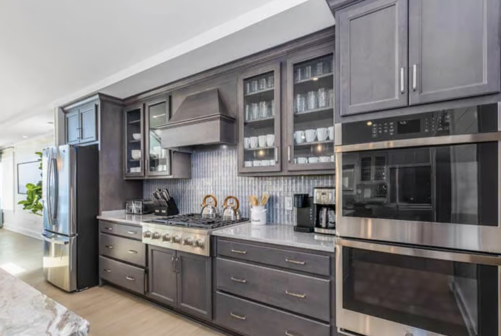 Modern kitchen with gray cabinetry, stainless steel appliances, a gas stove, glass-front upper cabinets, and a tiled backsplash.