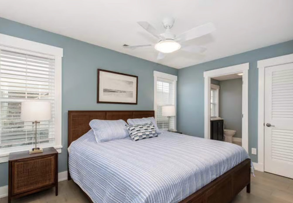Bedroom with blue walls, large bed with striped bedding, two bedside tables with lamps, and an en-suite bathroom.