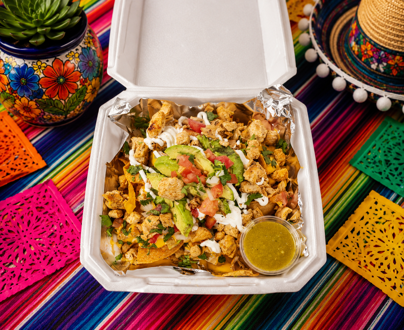Loaded chicken nachos, topped with avocado, tomatoes, sour cream, and cilantro, with a side of green salsa