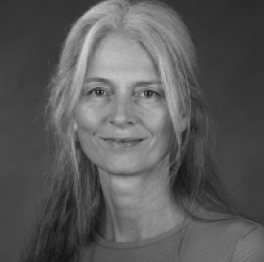A black and white image of Sandy Litchfield wearing a light colored tshirt and has lighter hair framed around the face going below the shoulders. Some of the hair is pulled back