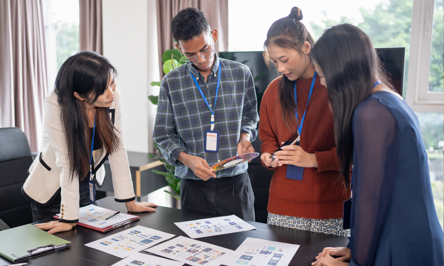 Four diverse professionals collaborating around a table with design mockups and charts in a modern office.