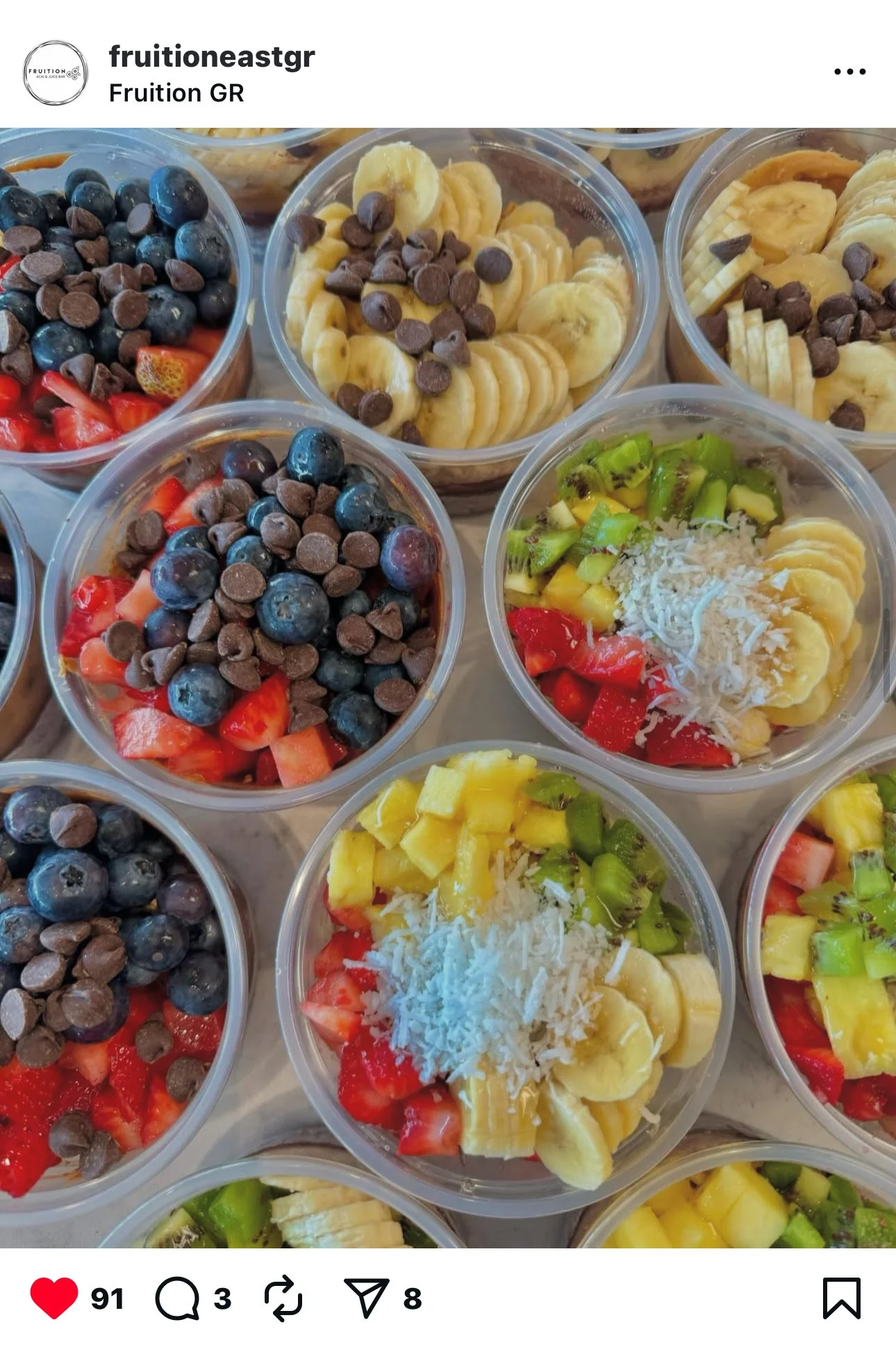 Multiple cups of fresh fruit bowls featuring strawberries, blueberries, bananas, kiwis, mango, and shredded coconut, topped with chocolate chips.