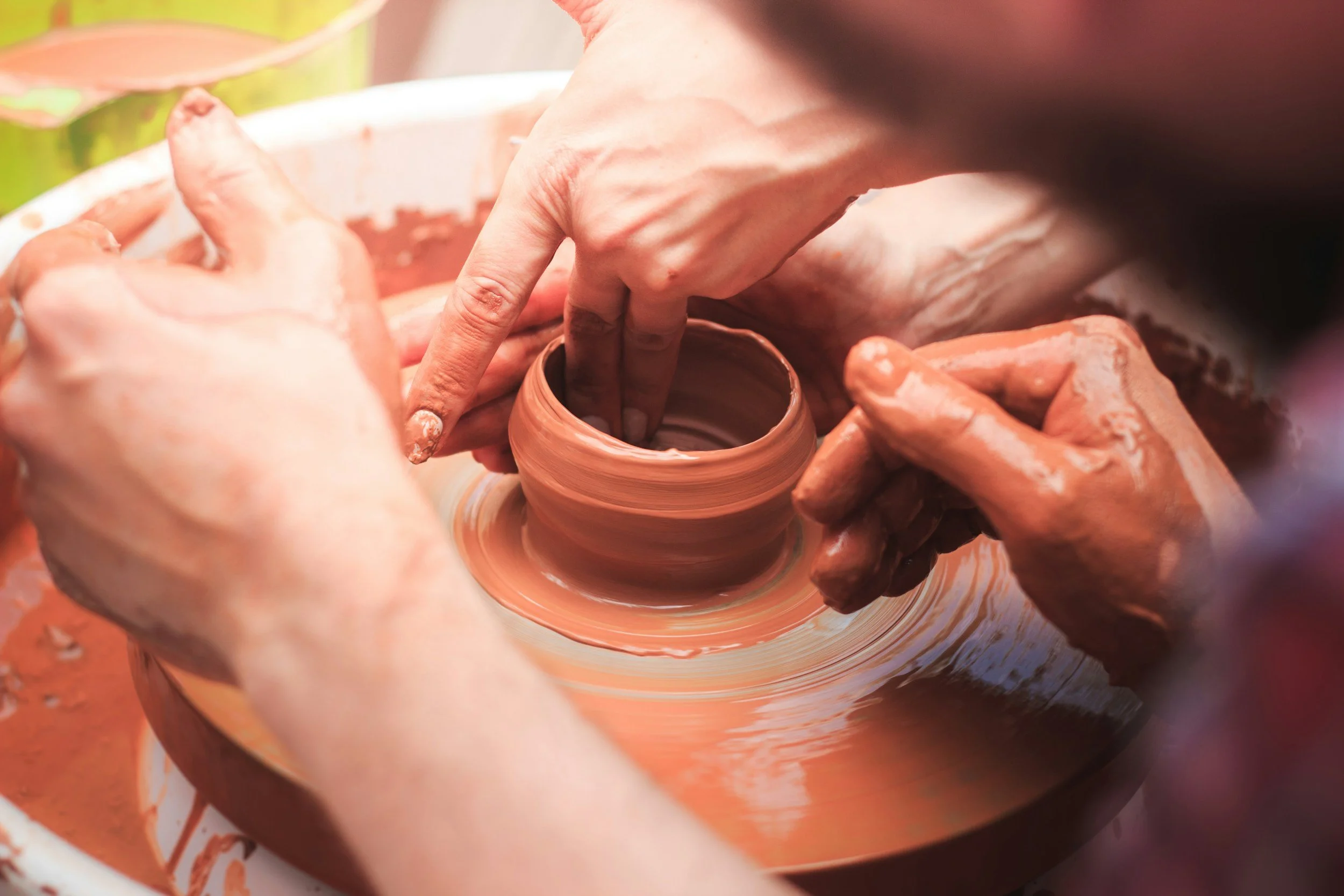 Multiple hands shaping and molding clay on a pottery wheel in a ceramics studio.