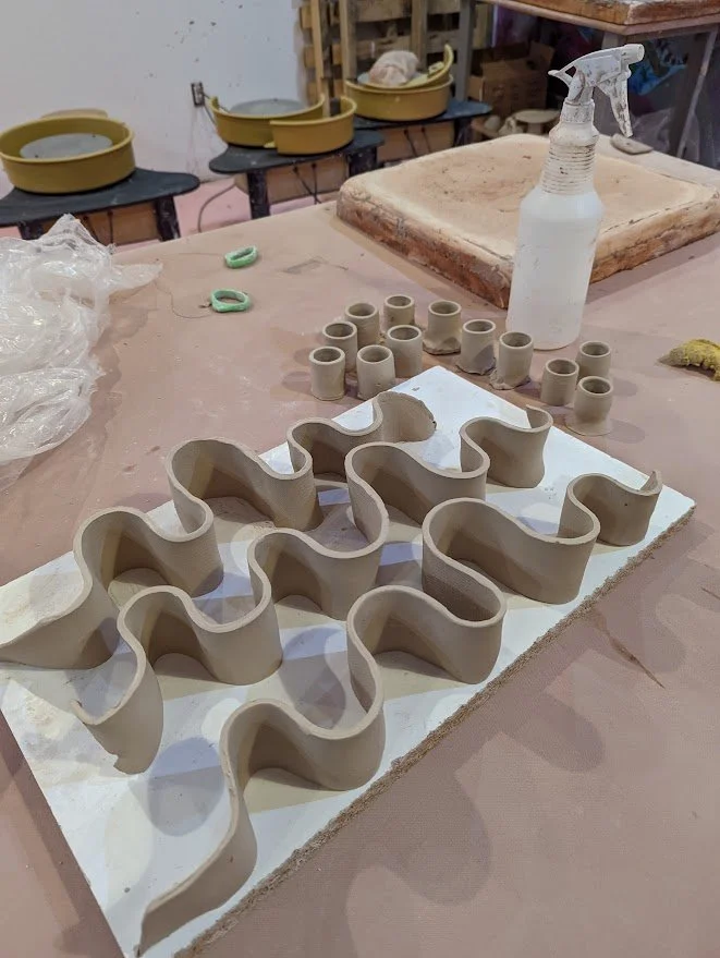 Clay pottery molds and small cylindrical clay pieces on a work table in a pottery studio.