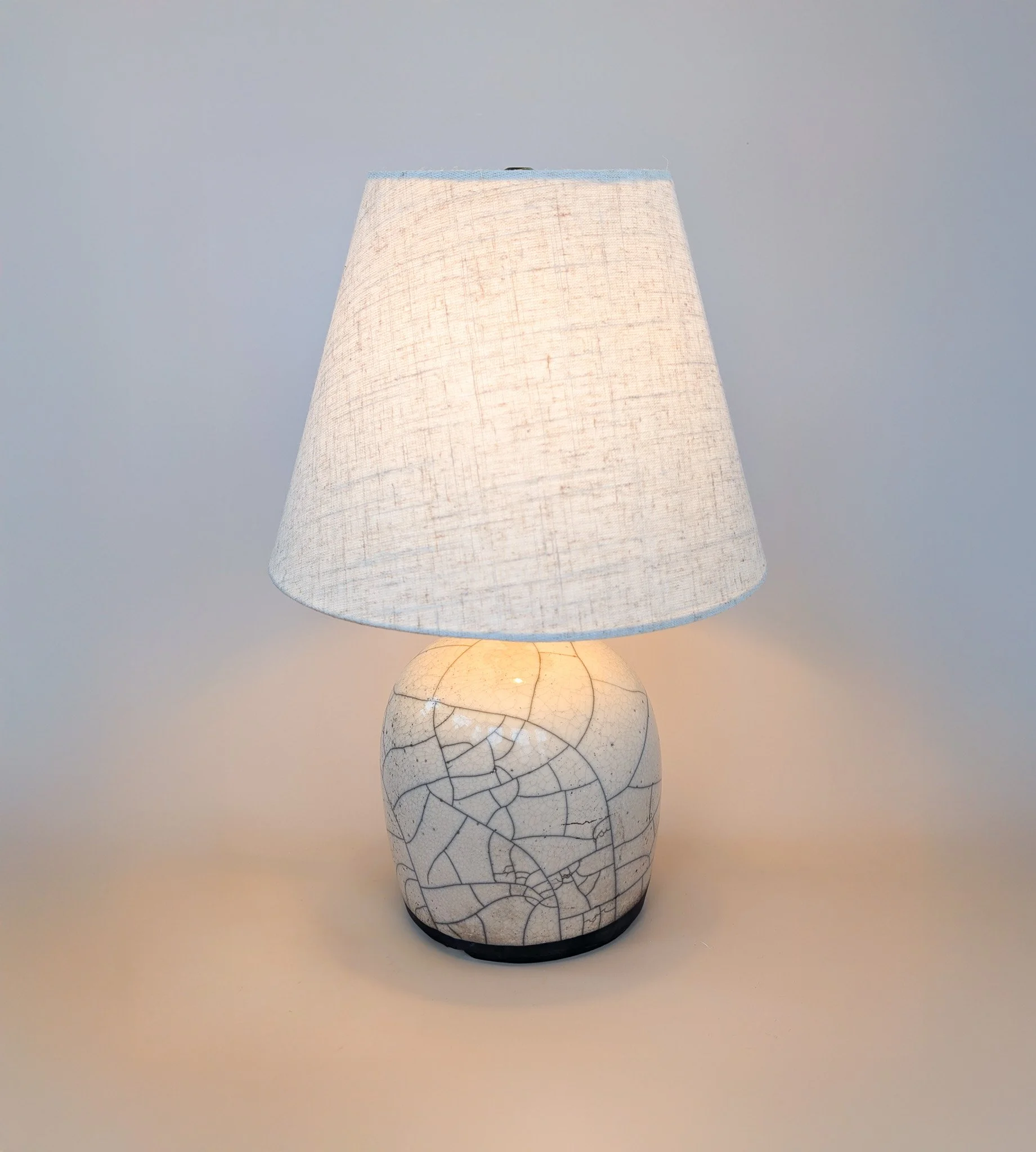 Ceramic table lamp with a cracked pattern and a fabric lampshade, turned on with a warm light.