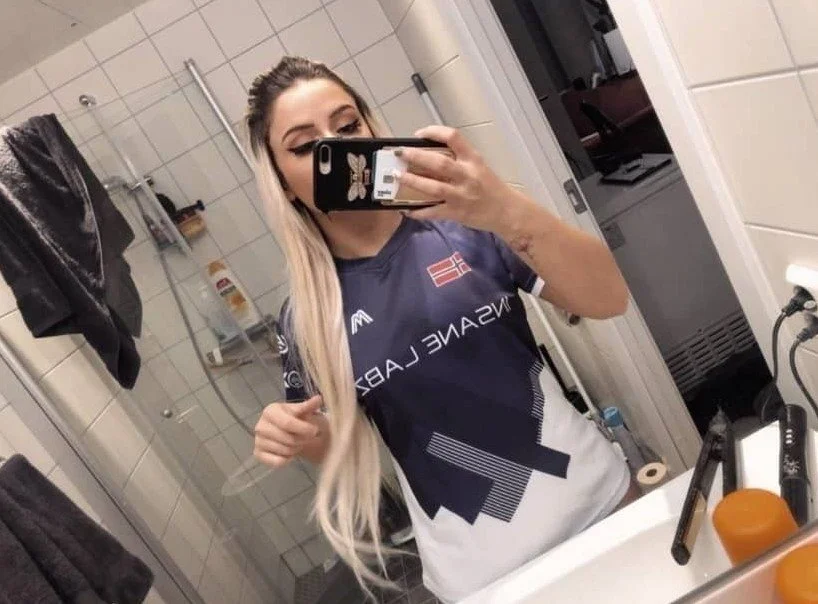 Ailincia / Arjeta tar et speilbilde med telefonen sin på badet iført en blå Major Militia jersey. Hun er en twitch streamer og streamer Valorant. 