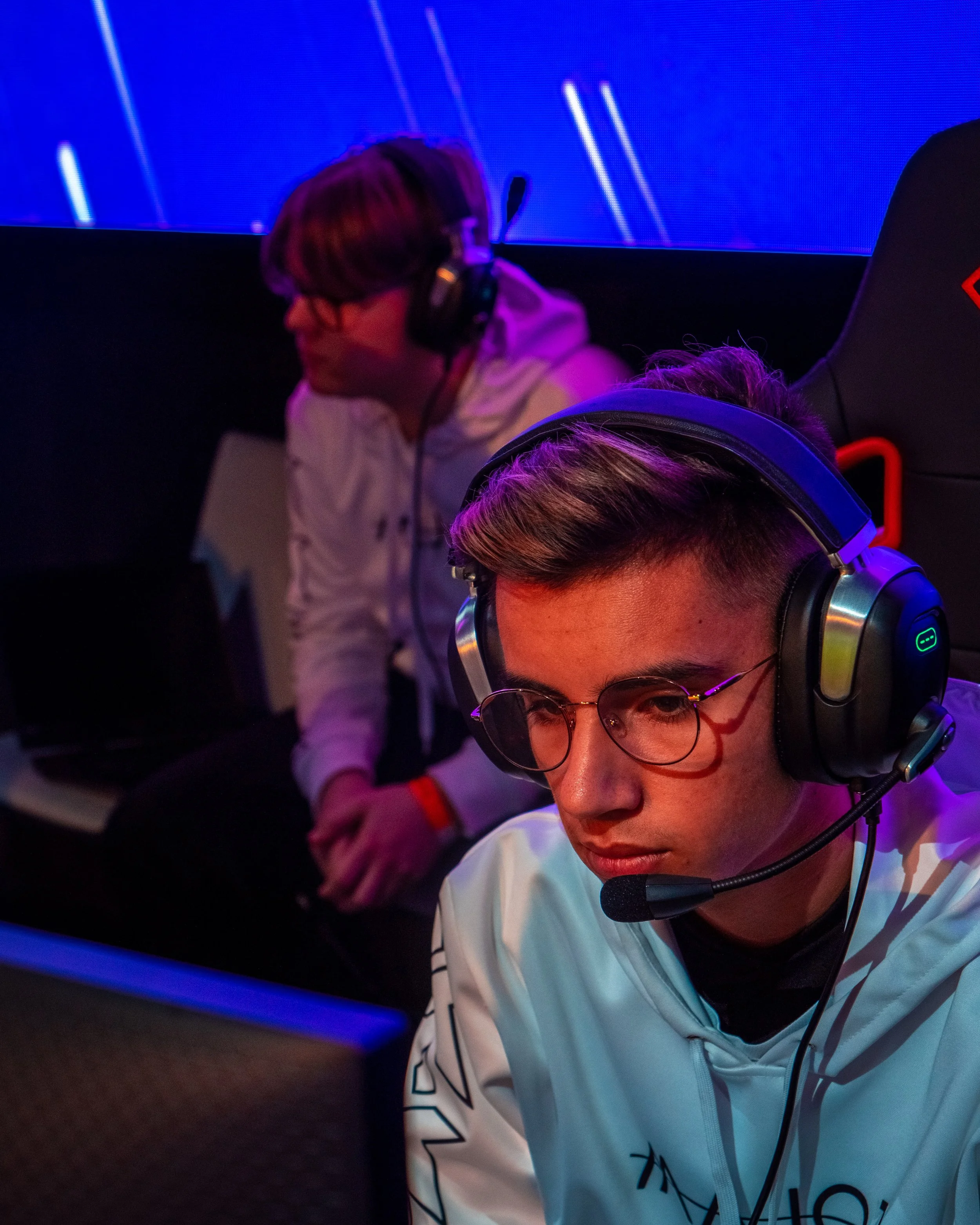 To unge menn med hodetelefoner som spiller dataspill i et miljø med blå og lilla lys.