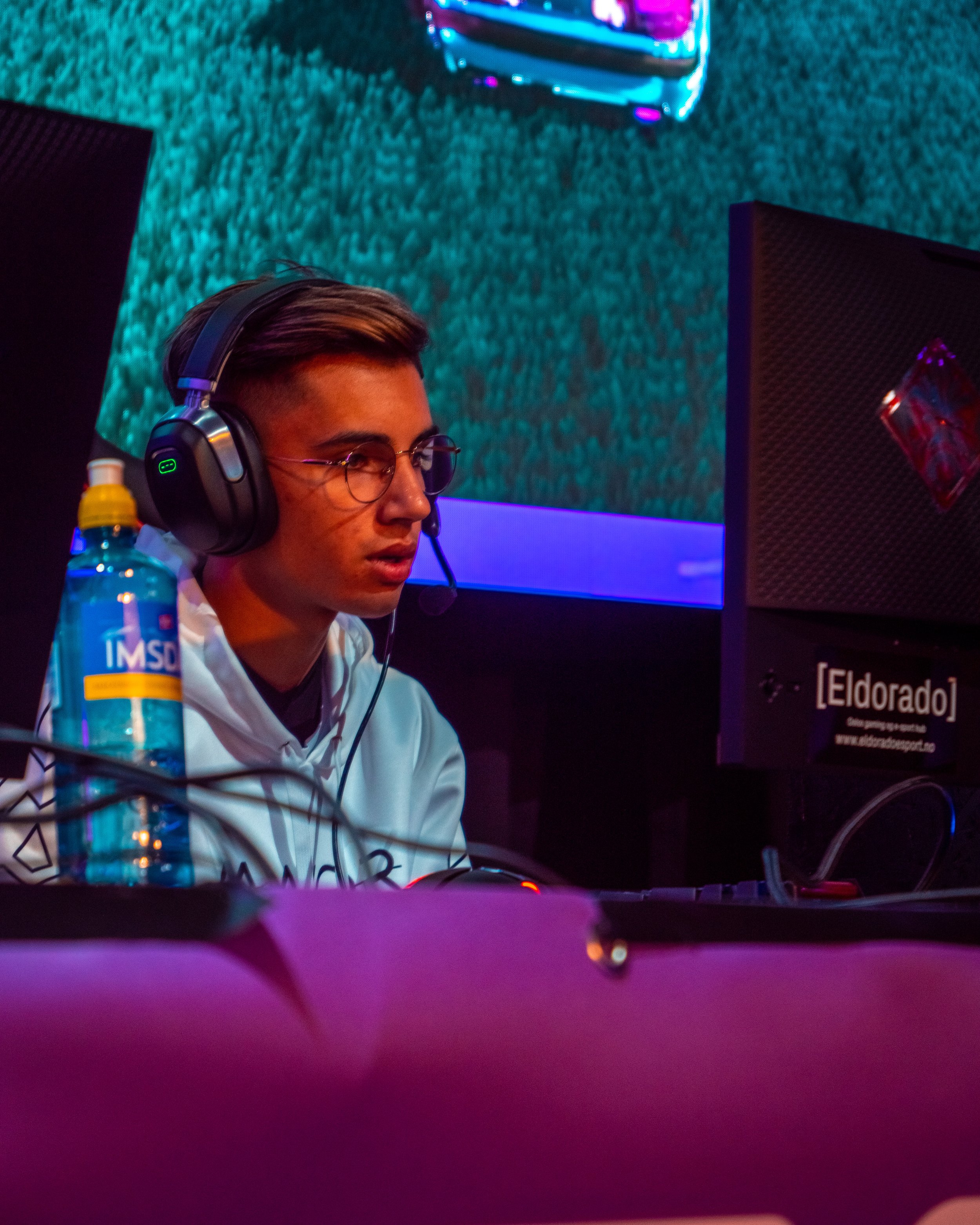 En ung mann som spiller dataspill med headset, omgitt av farget belysning.