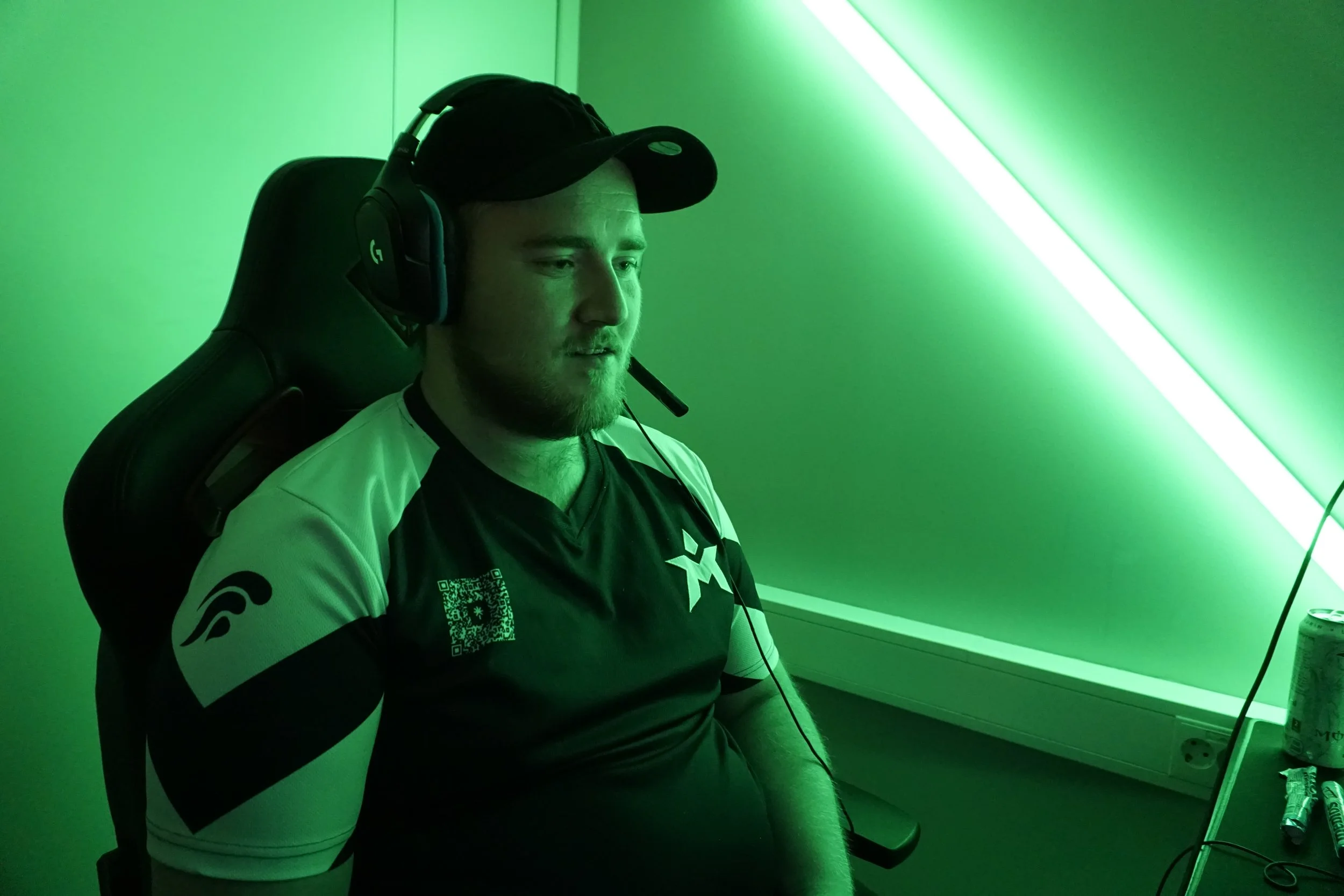 En mann som spiller dataspill med gaming-headset, sittende i en stol, i et rom med grønn barget lys.