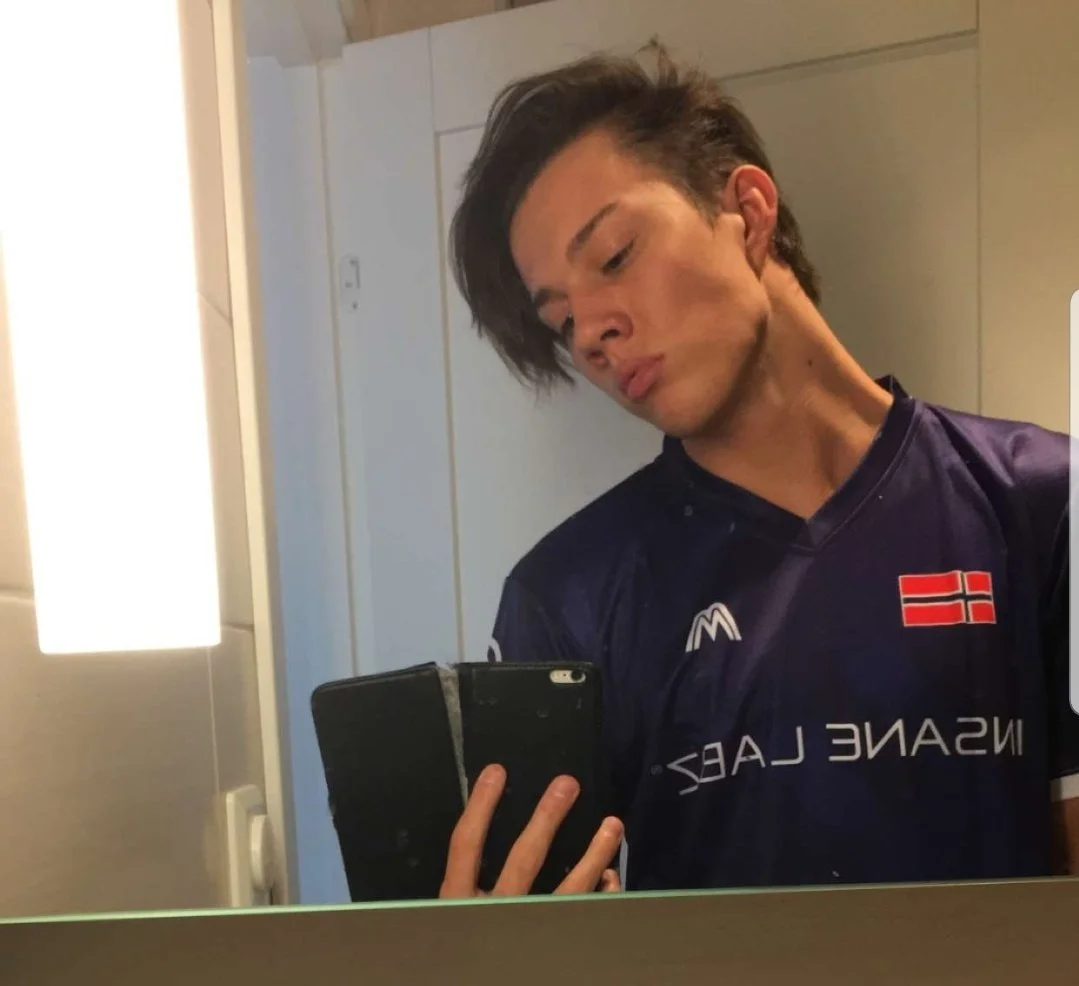 En ung mann tar en selfie i speilet. Han har mørkt, stygt hår og er iført en norsk fotballdrakt.