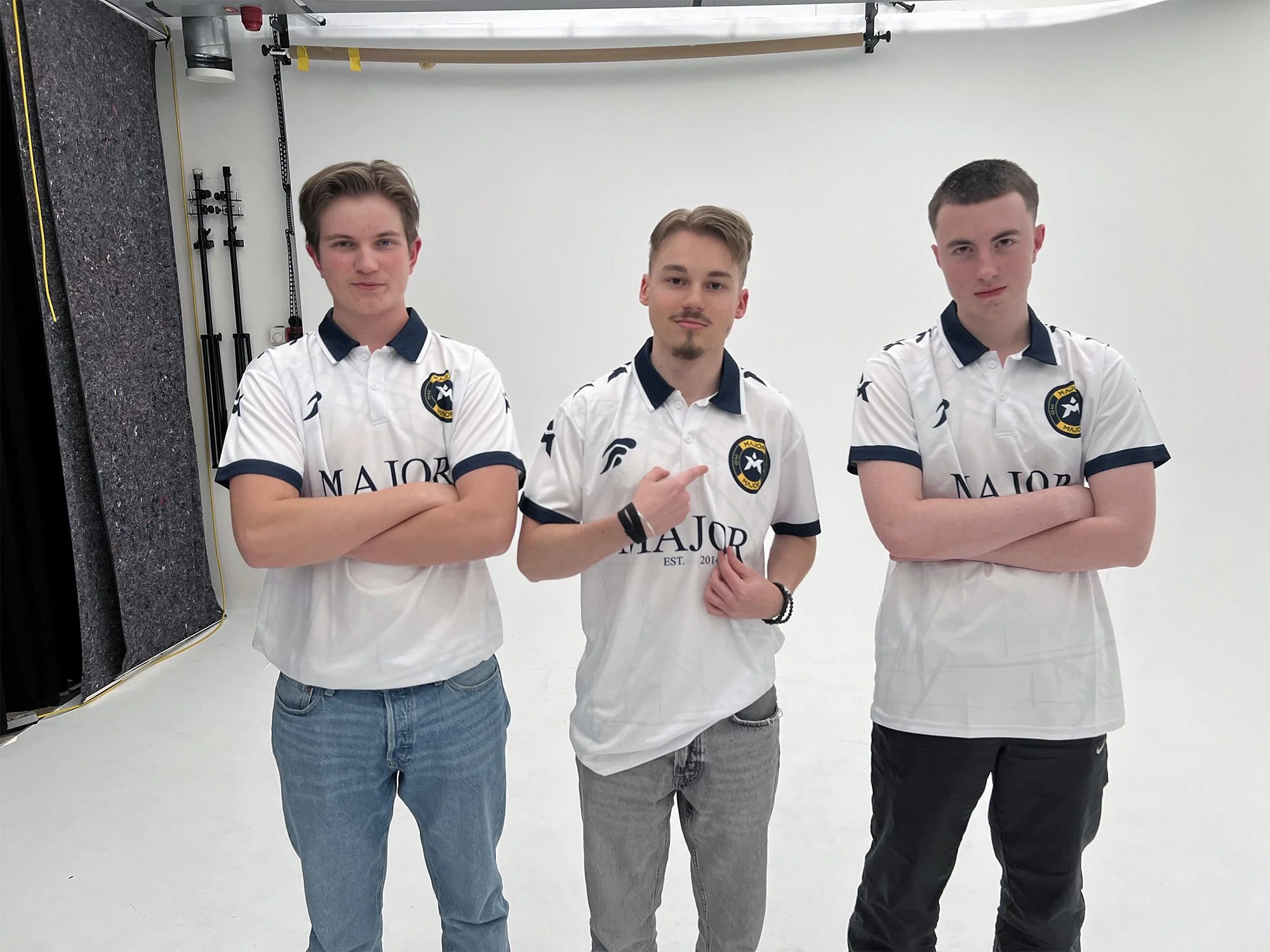 Tre unge menn står i en fotografi i en studio, alle iført hvite fotballdrakter med logo og teksten 'Major'.