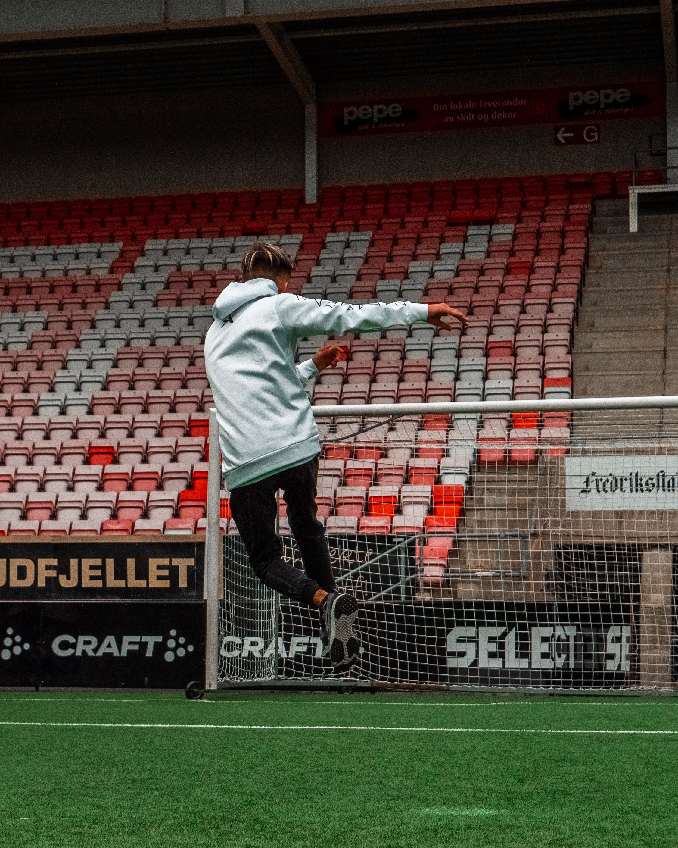 En person som hopper i en fotballmålsbue på en fotballbane med tomme seter i bakgrunnen.