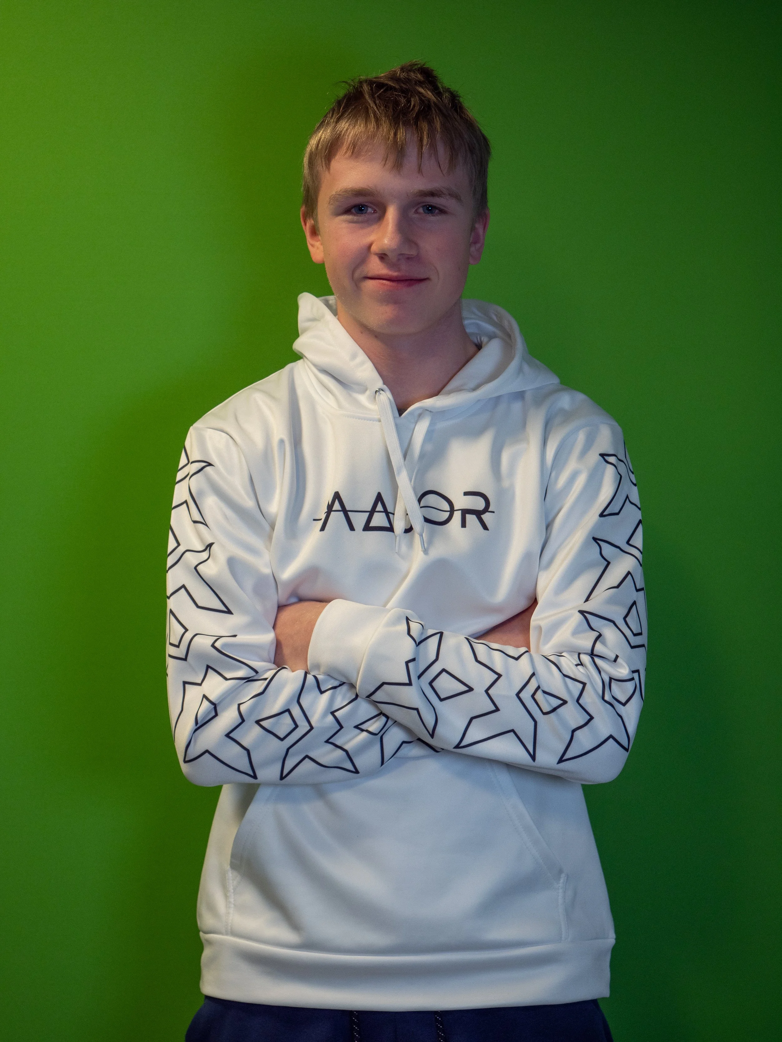 En ungdom med armene crosses står foran en grønn bakgrunn iført en hvit hettejakke.