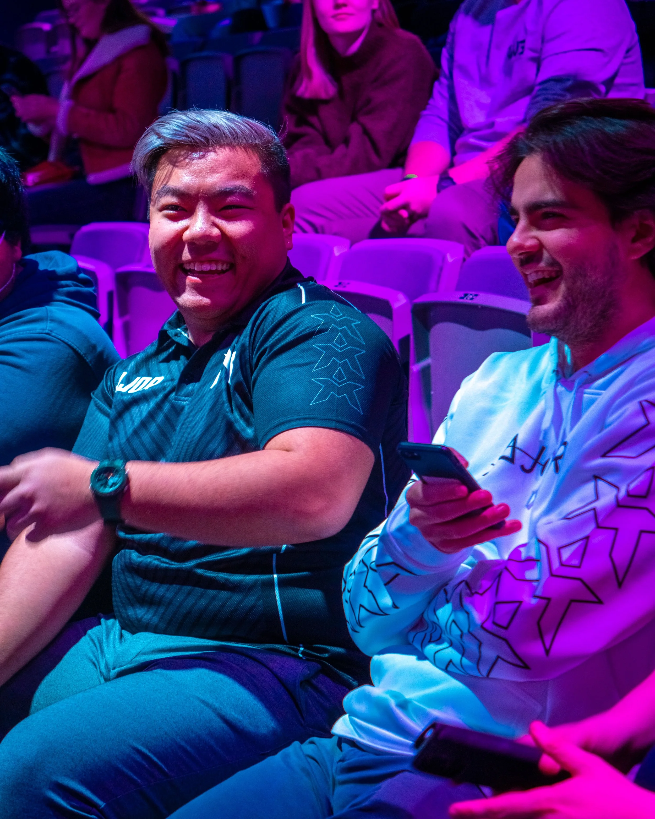 To personer som ler og har det gøy under en begivenhet, med andre mennesker i bakgrunnen.