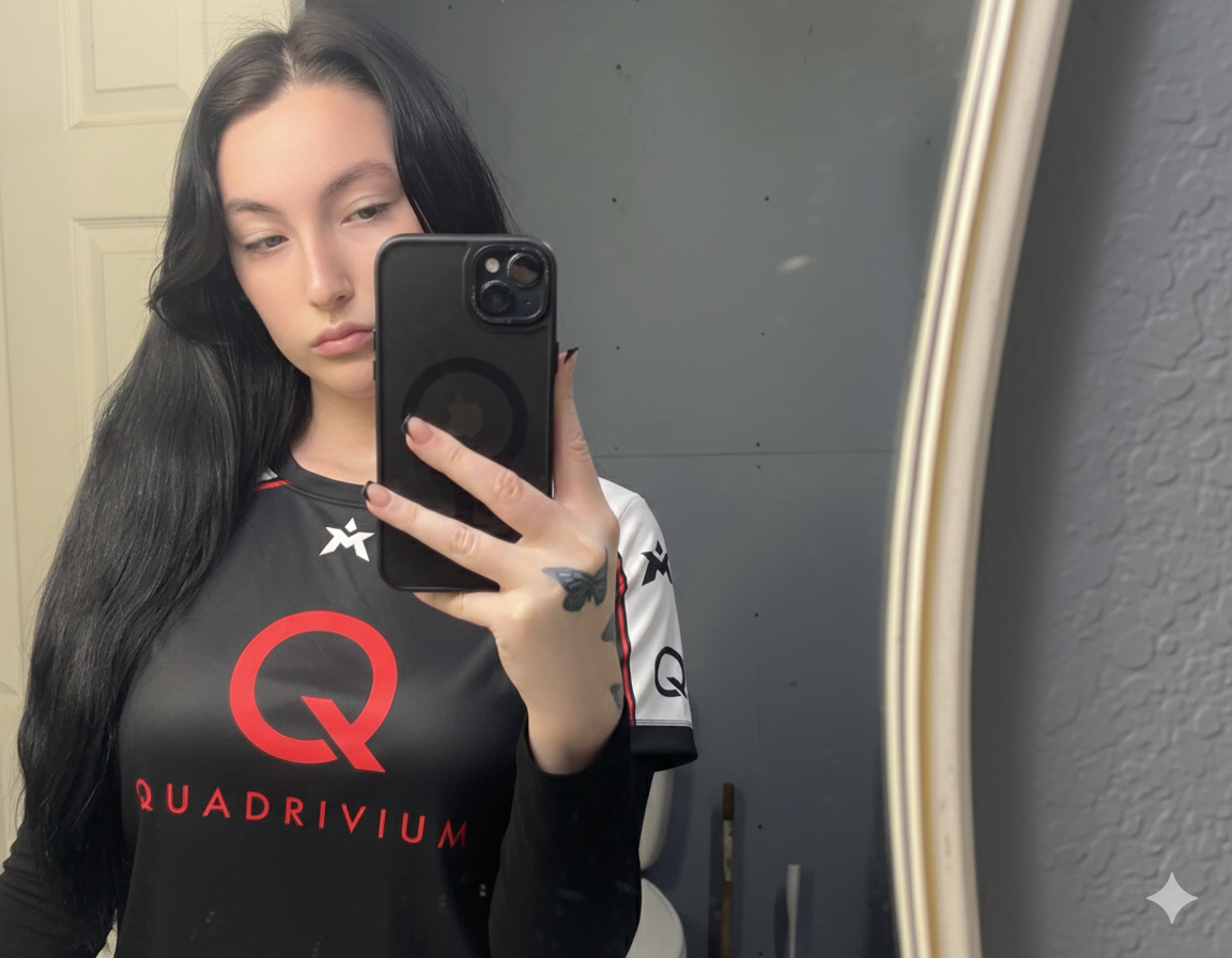 En ung kvinne tar et speilbilde av seg selv med mobiltelefon i et rom. Hun har lang svart hår og på seg en svart og hvit sportsklær med logo og teksten QUADRIVIUM.
