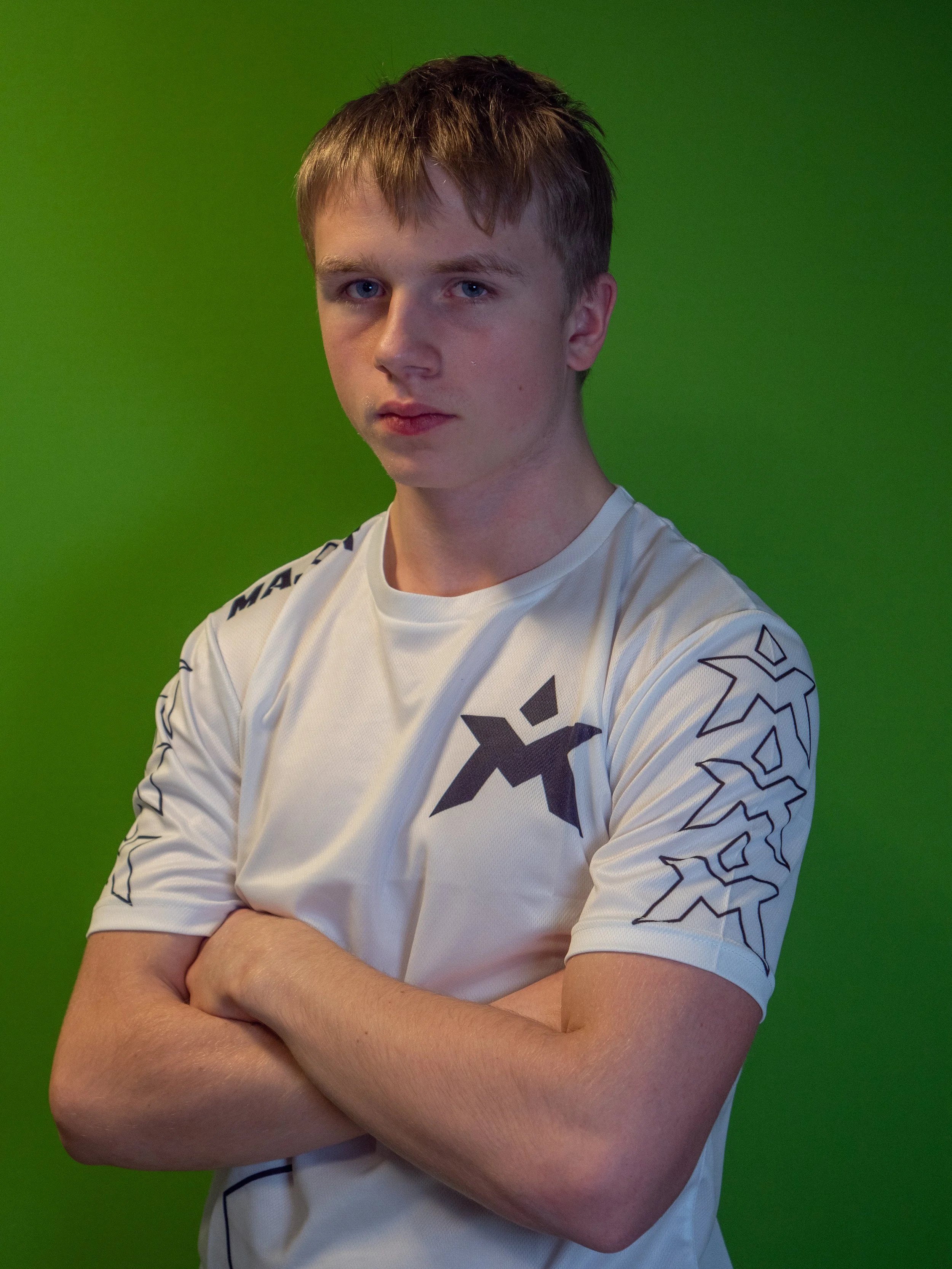 Ung mann med kort brunt hår, blonde øyne, som står med armene korslagt foran en grønn bakgrunn, iført en hvit sportsgenser med svart logo og linjer på ermene.