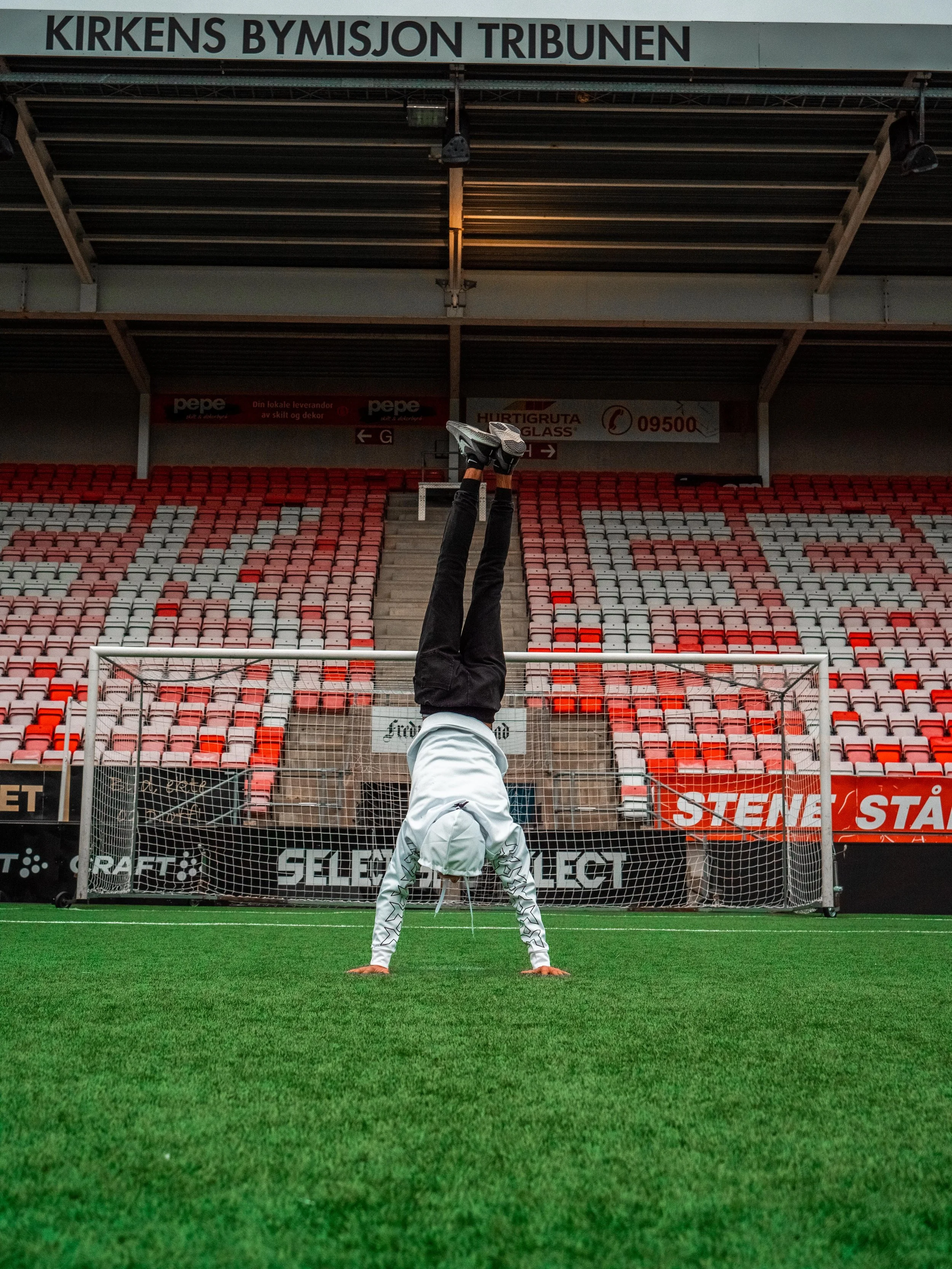 Person som står på hender på en fotballbane med et mål i bakgrunnen i en fotballstadion.