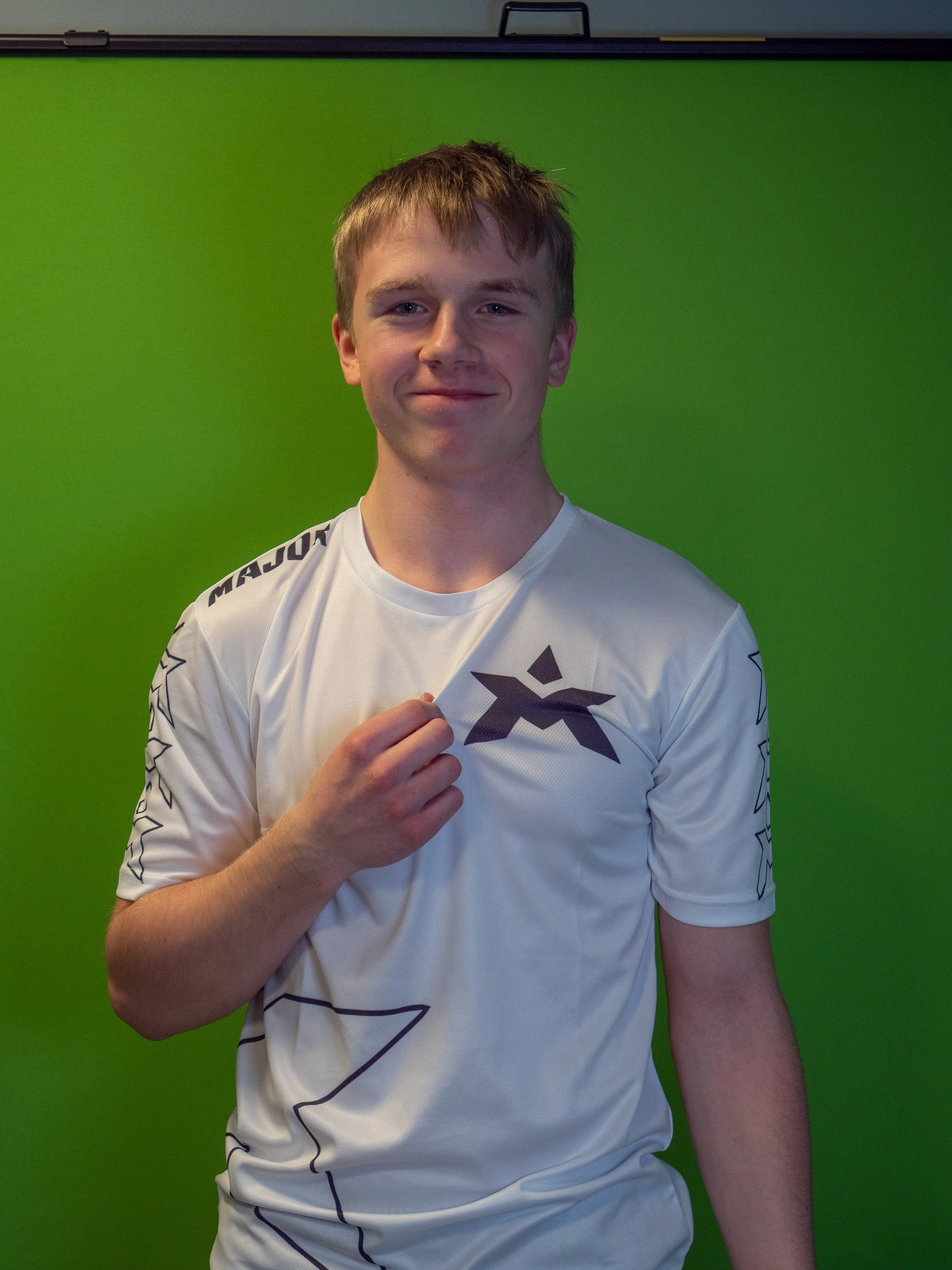 Ung mann som smiler og holder opp trøyen sin foran en grønn bakgrunn.