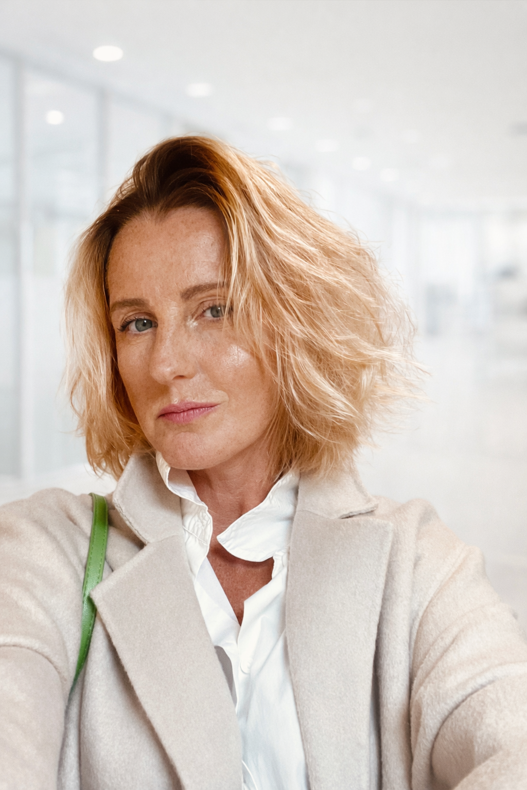 Une femme aux cheveux roux bouclés prenant un selfie dans un environnement lumineux et moderne.
