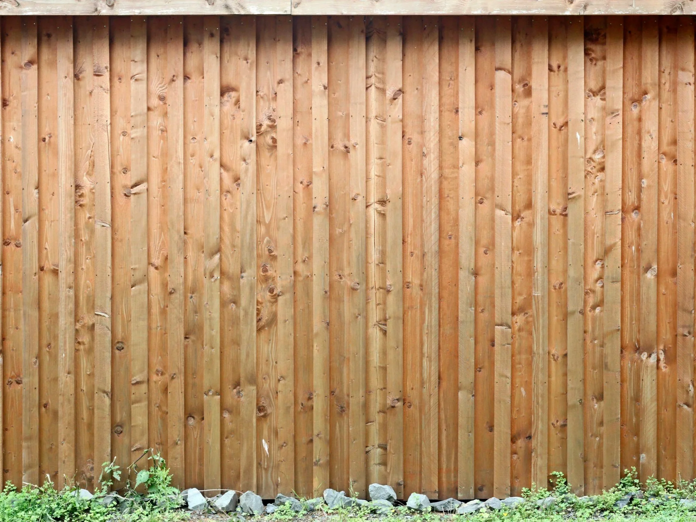 Wooden backyard fence with rocks and small plants at the base. waterloo region fencing installation and repair