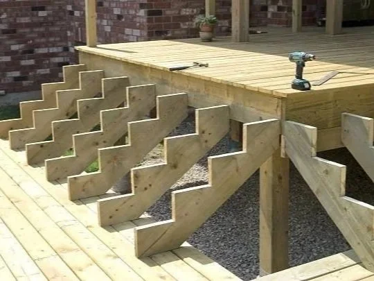 L-shape wooden deck with attached zigzag support beams and a cordless drill on top. Waterloo region decking design and repair