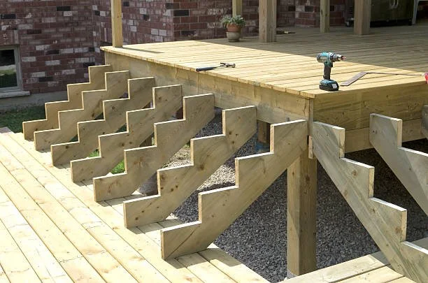 L-shape wooden deck with attached zigzag support beams and a cordless drill on top. Waterloo region decking design and repair
