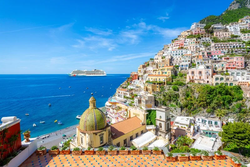 Norwegian Cruise Line ship anchored near a vibrant Mediterranean coastal town with terraced buildings and seaside views