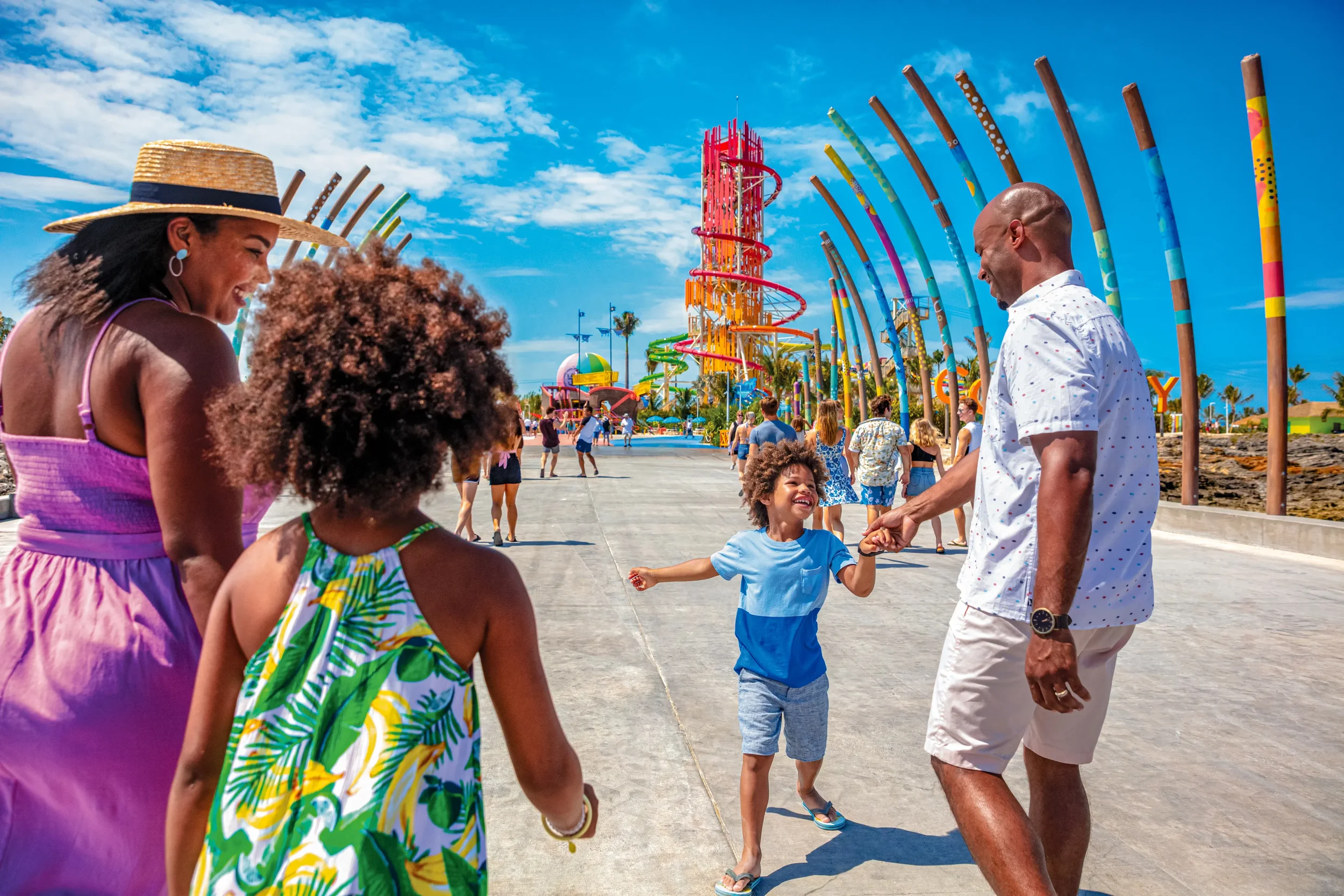 Family arriving at Perfect Day at CocoCay in the Bahamas, walking along the pier entrance with Daredevil’s Tower water slide visible in the background on Royal Caribbean’s private island.