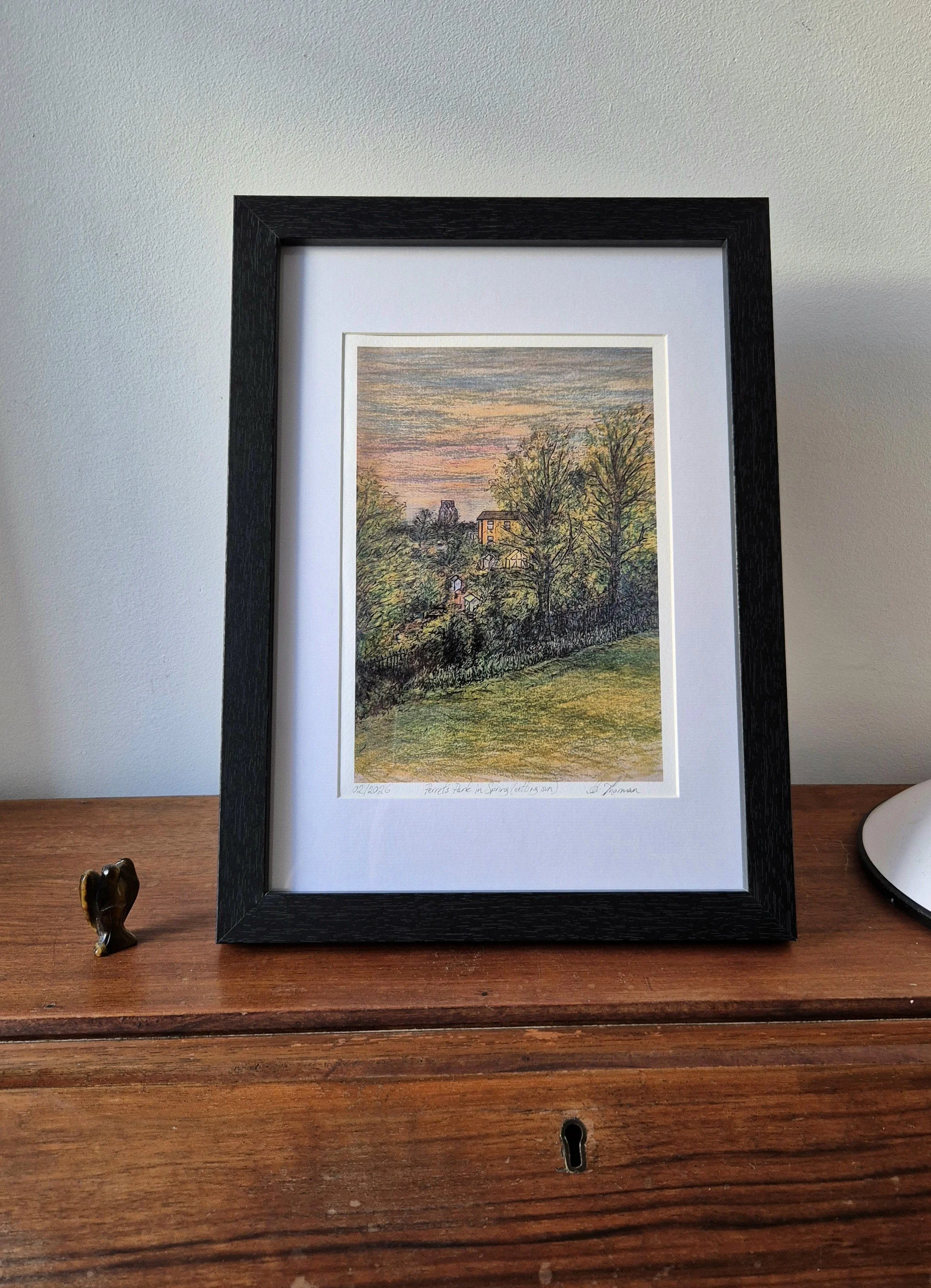 A picture of a framed print on a bureau next to a small figurine