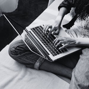 Person sitting on a bed using a laptop, with one hand on the keyboard.