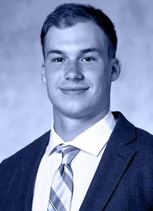 Young man in a suit with a tie, smiling, in a professional portrait.