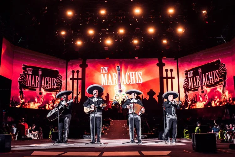 Mexican musicians wearing traditional Mariachi outfits playing instruments on stage during a performance at a Mariachi event.