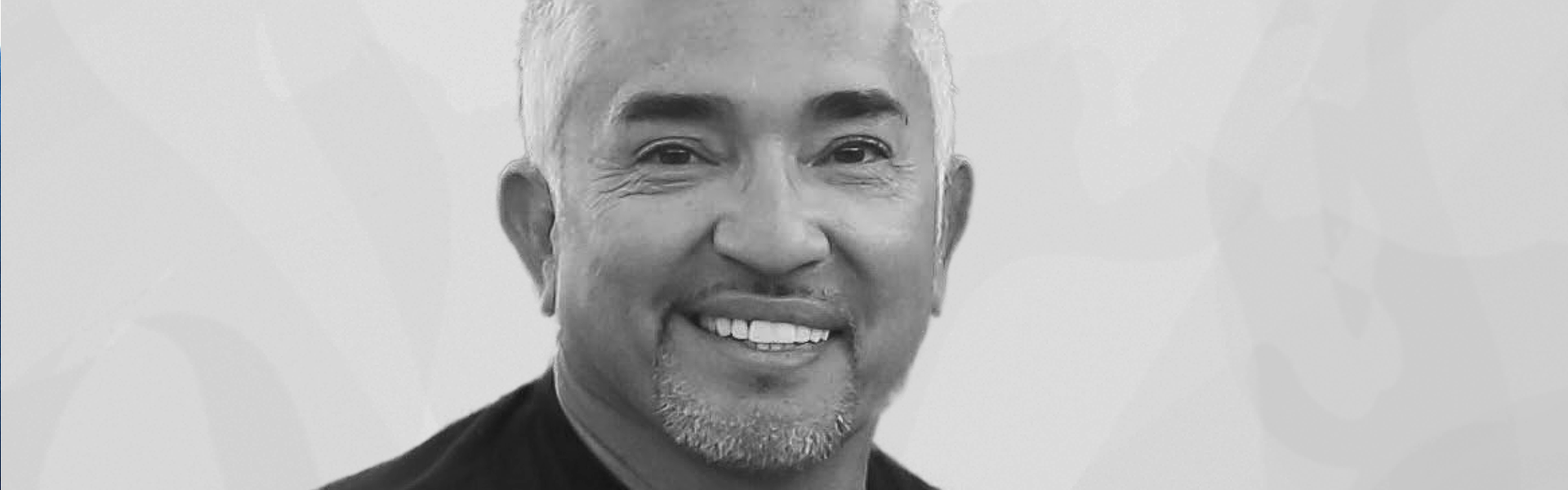 A smiling man with white hair and a goatee, wearing a dark shirt, against a light background.