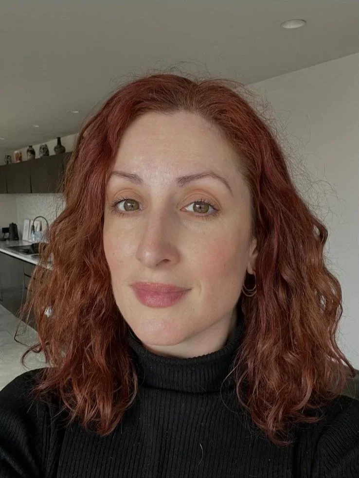 A smiling woman with a roll neck top, standing in a kitchen.