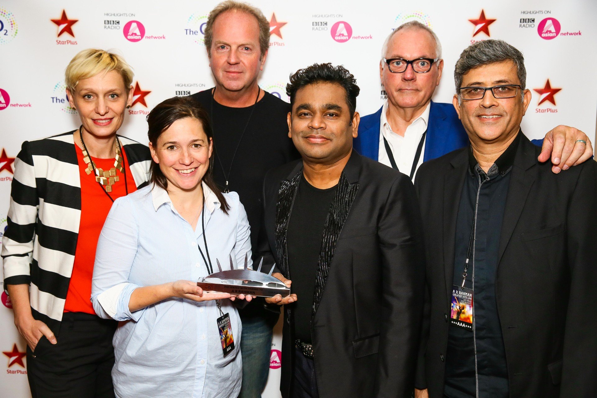 Six people standing together at an event, with a woman in the front holding an award and smiling.