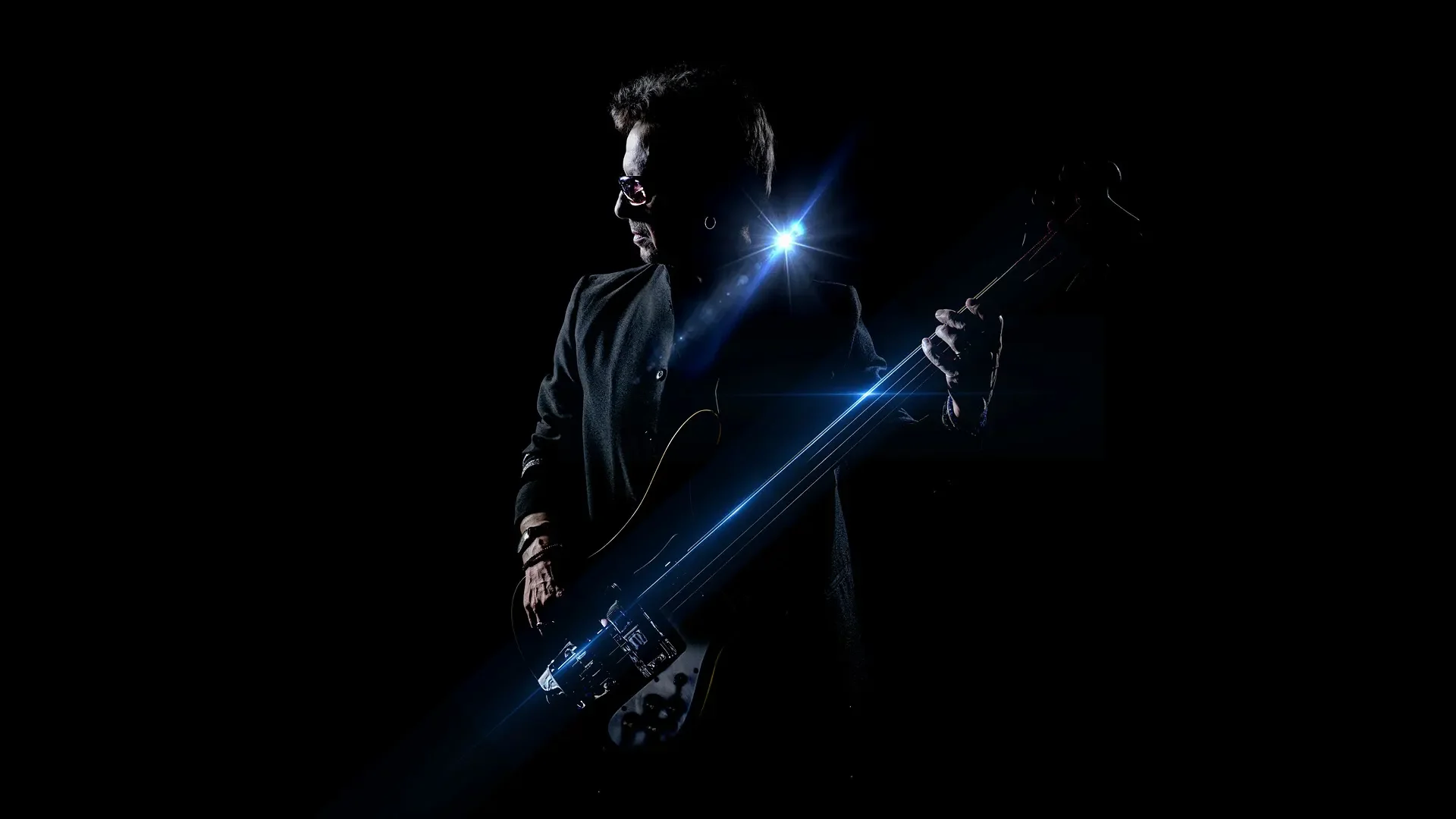 Silhouette of a man playing an electric guitar in a dark setting with bright blue starburst light effects.