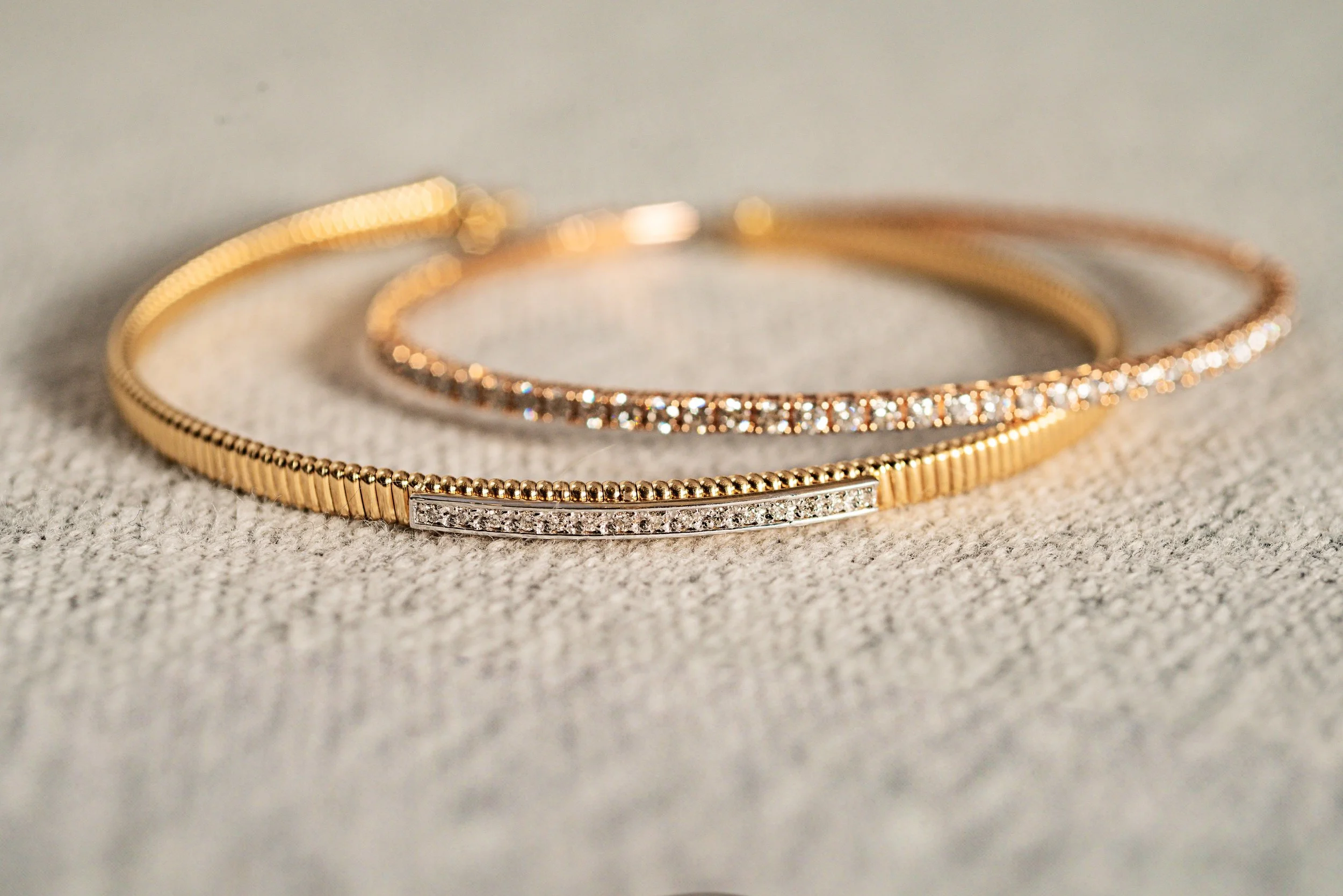 Tres pulseras delicadas de oro y plata con detalles de diamantes sobre tela gris