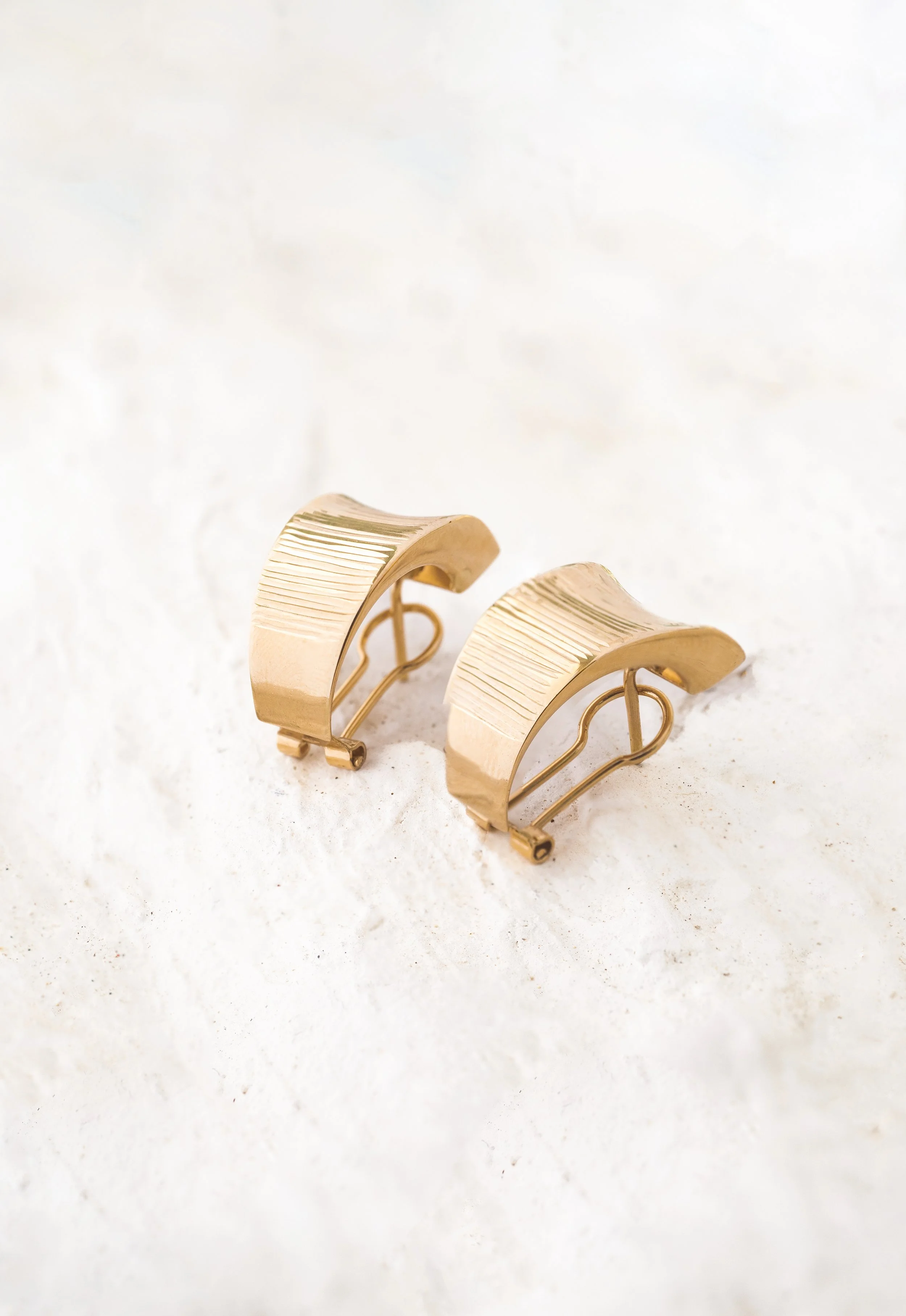 Aretes dorados con diseño de líneas rectas y curvadas, colocados sobre una superficie blanca