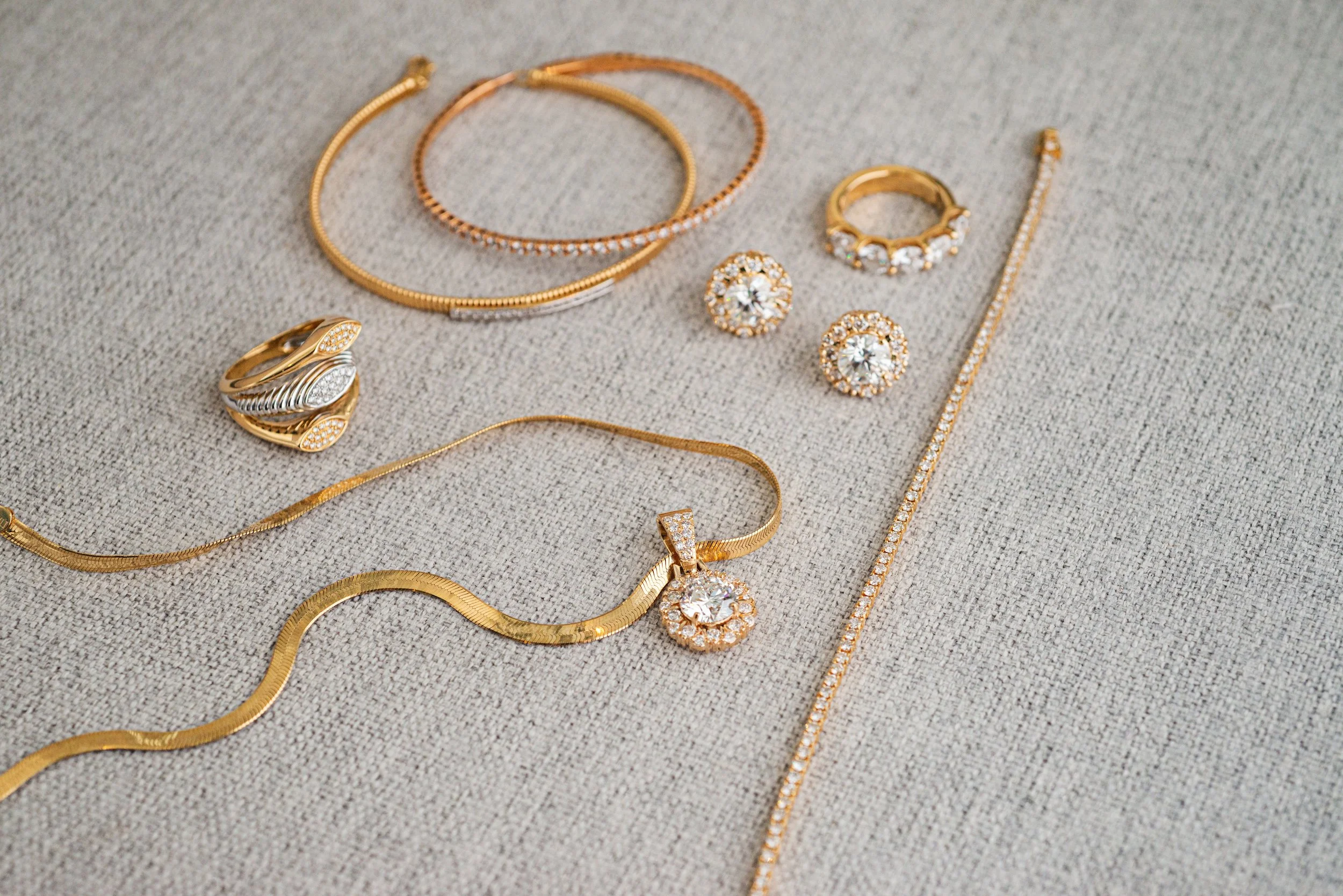 Joyería dorada y plateada, incluyendo collares, anillos, pendientes y una pulsera, dispuesta sobre tela gris.