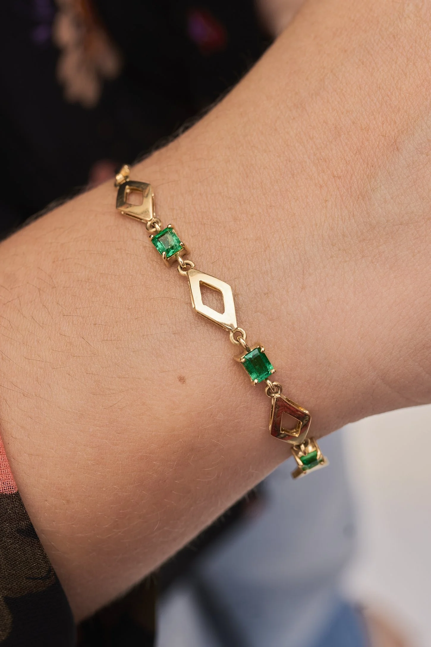 Pulsera de oro con esmeraldas y formas de rombo abiertas.