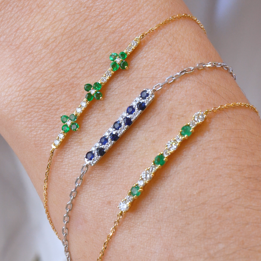 Tres pulseras en la muñeca con piedras preciosas esmeraldas, zafiros y diamantes en cadenas de oro y plata.