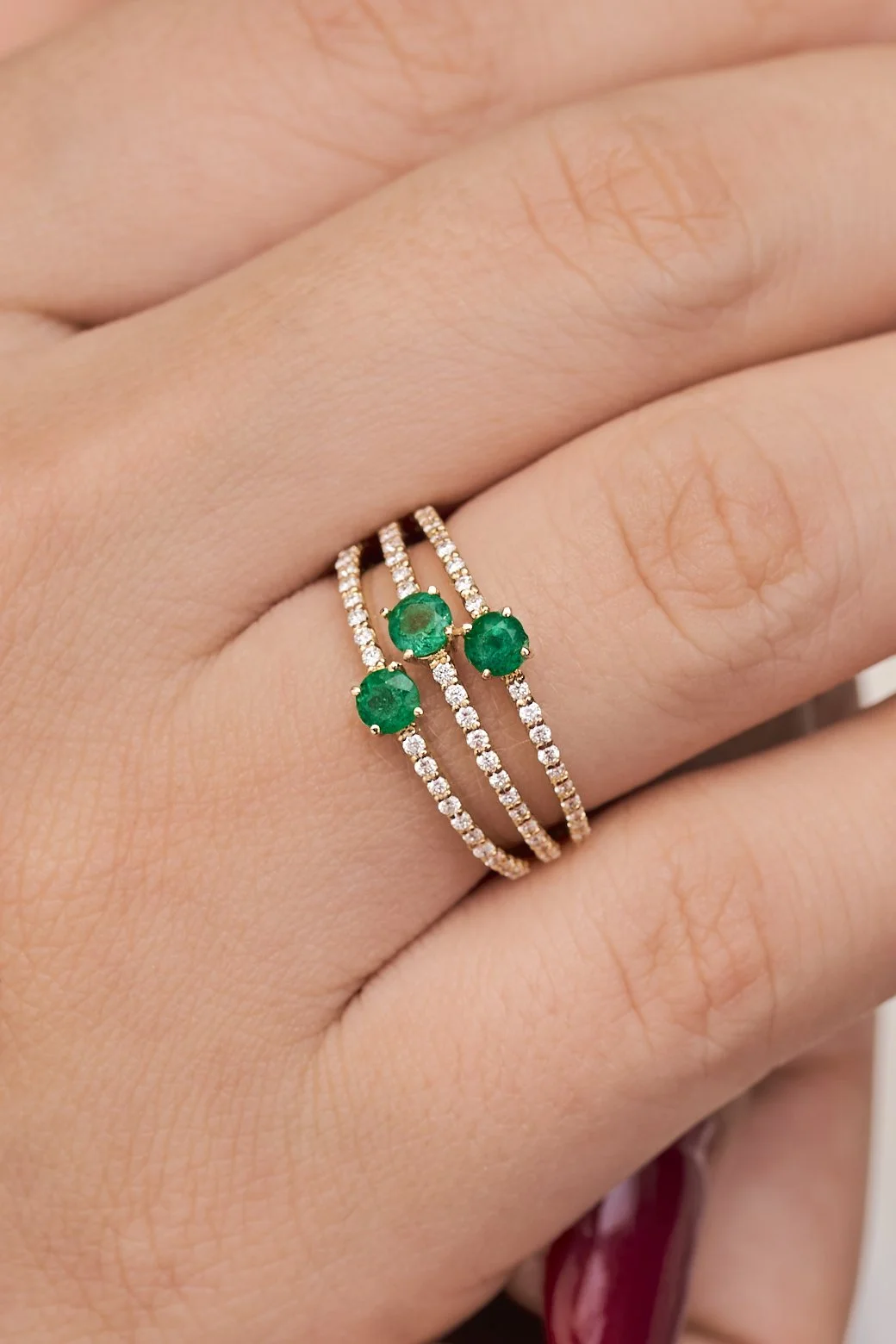Anillo de oro con tres esmeraldas y talle de diamantes en un dedo.